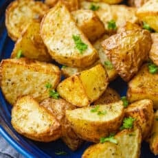 Close up of air fryer roasted potatoes on a blue platter, garnished with parsley.