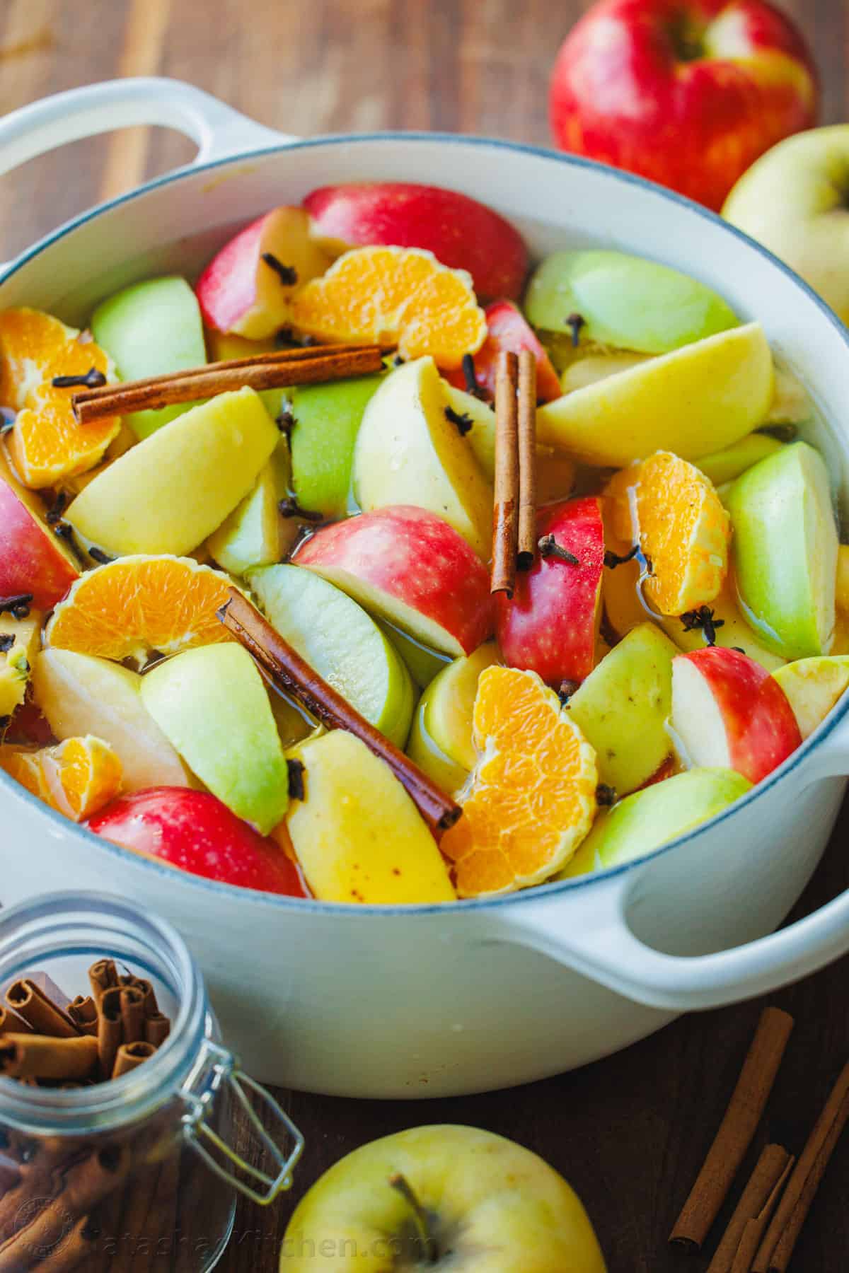 Apple cider ingredients in a pot ready to simmer on the stove. Colorful apples, cinnamon, oranges, cloves, sugar