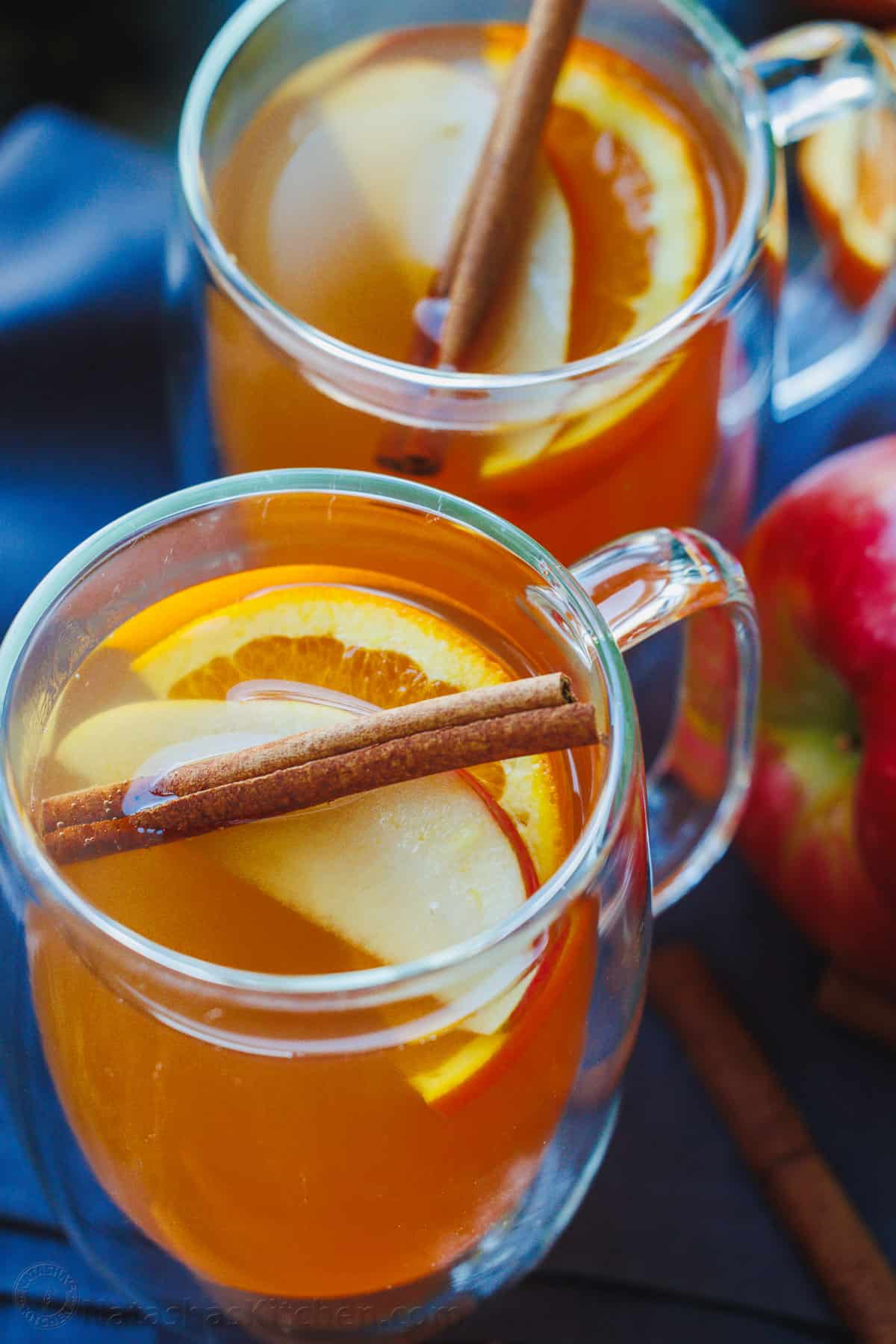 Apple cider garnished with apple and orange slices and a cinnamon stick. Served in a glass mug.