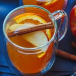 Warm apple cider in a mug with floating cinnamon stick and apple and orange wedges