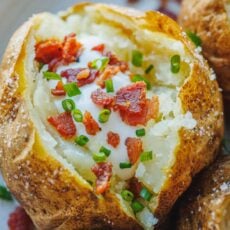 Close up view of a perfect baked potato topped with sour cream, bacon, and chives.