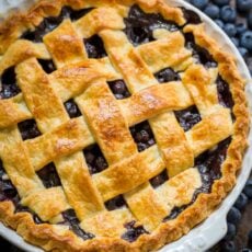 Blueberry pie with lattice crust, surrounded by fresh blueberries