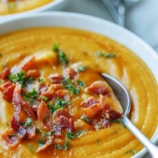 A bowl of homemade butternut squash soup garnished with bacon and parsley, with a spoon.