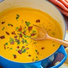 Creamy carrot soup in pot garnished with bacon and parsley