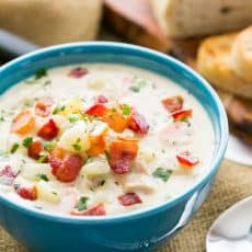 A bowl of New England clam chowder with a spoon beside it and bread behind it