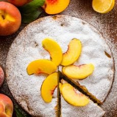 Fresh peach cake with one slice to serve. Decorated with powdered sugar and fresh peach slices