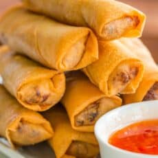 Egg rolls stacked on platter with dipping sauce
