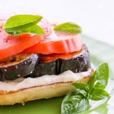An open-faced eggplant and tomato sandwich garnished with basil on a green plate