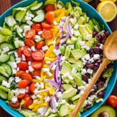 Greek salad ingredients arranged in mixing bowl with greek salad dressing on the side