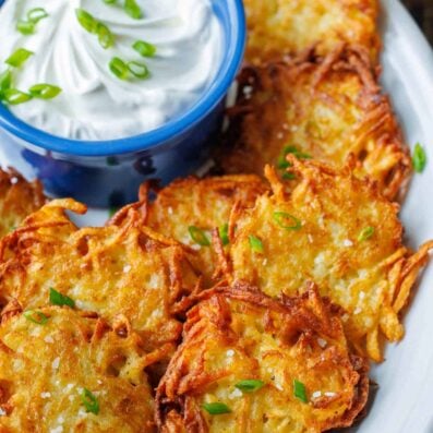 Latkes fried and topped with chives. On a plate with sour cream