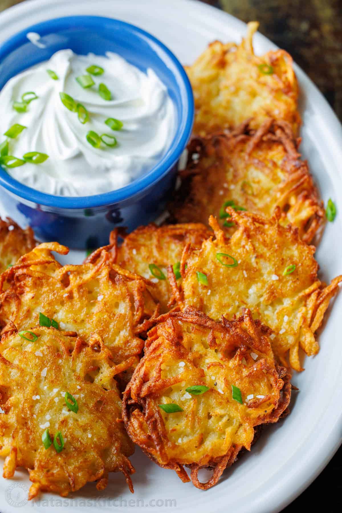 Latkes fried and topped with chives. On a plate with sour cream
