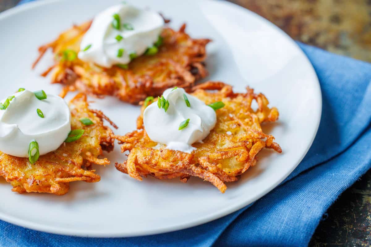 three latkes on a plate with a dollop of sour cream and sprinkled with fresh chives