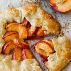 Peach galette on parchment paper with fresh peaches