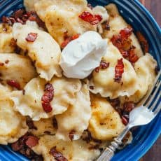 A batch of potato pierogi in a bowl topped with bacon and sour cream