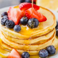Ricotta Pancakes stacked on plate with fruit and drizzled with maple syrup