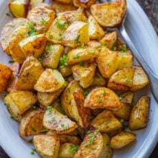 Overhead view of perfect roasted potatoes in a white serving dish, garnished with parsley.