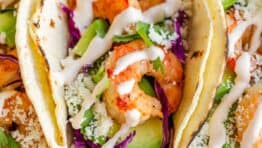 Shrimp taco up close on platter drizzled with sauce